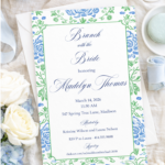 Blue and green floral invitation styled on linen with soft blue ribbon, flowers, and elegant bridal shower flatlay styling