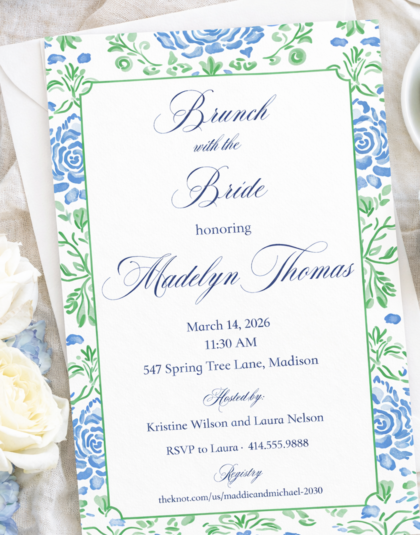 Blue and green floral invitation styled on linen with soft blue ribbon, flowers, and elegant bridal shower flatlay styling