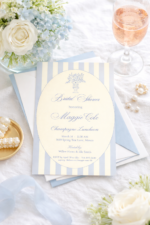 Printed blue striped bridal shower invitation on white linen table with soft blue hydrangeas, rosé champagne glass, pearl jewelry, and gold dish styling