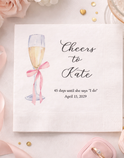 pink bow on champagne glass with names on personalized cocktail napkin for bridal shower